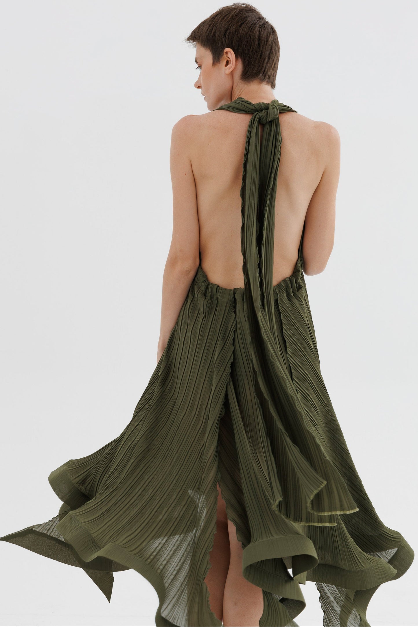 Woman wearing a green pleated dress with a halter neck design on a white background