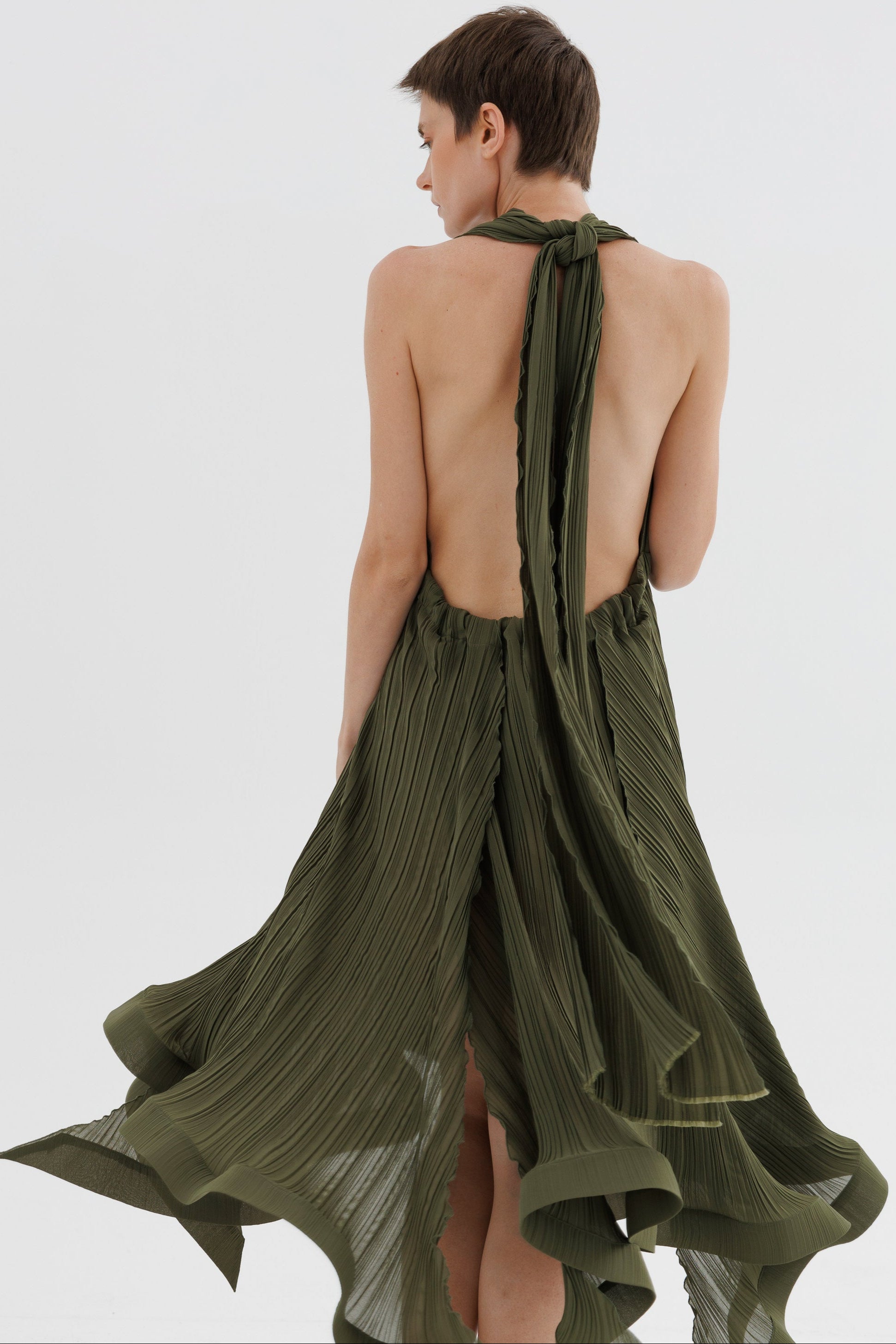 Woman wearing a green pleated dress with a halter neck design on a white background